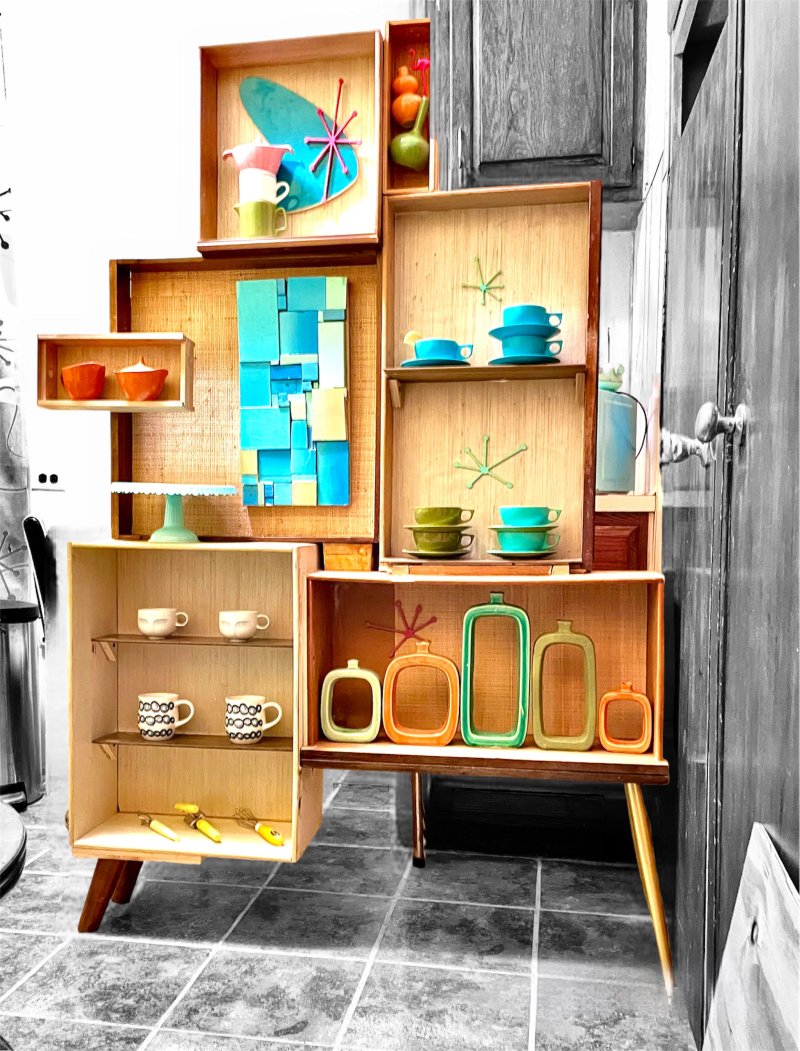 Freestanding shelf wall Jason built from found wooden drawers on splayed legs, backed with grasscloth and filled with atomic-era ceramics